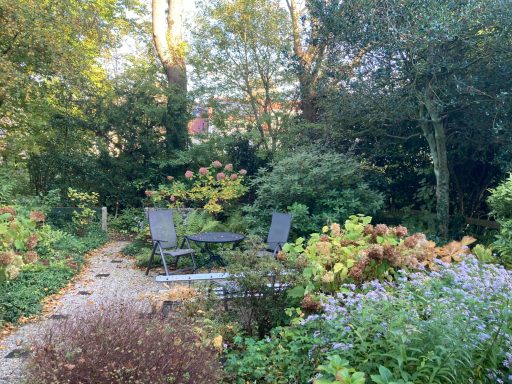 Tuin met comfortabele stoelen en tafel omringd door planten en bloemen.